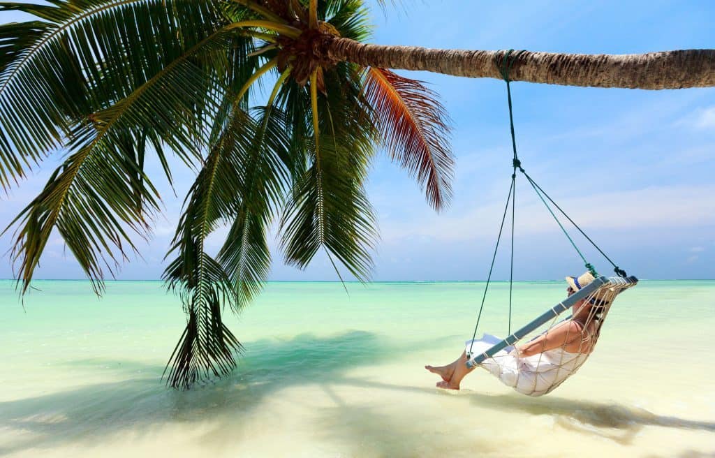 Woman in swing under palm tree with ocean view arrange with luxury travel agents