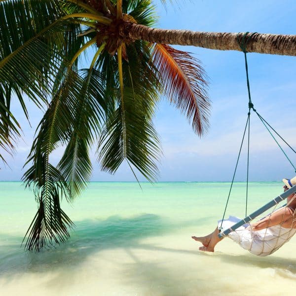 Woman in swing under palm tree with ocean view arrange with luxury travel agents
